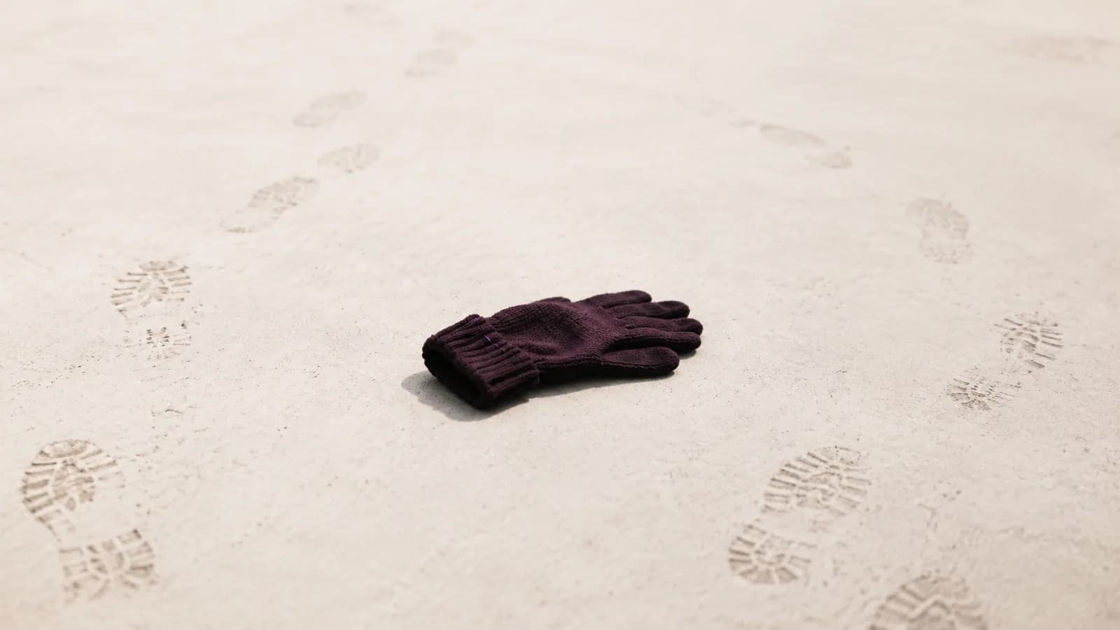 A single dropped glove on an empty pavement with footprints passing around it.