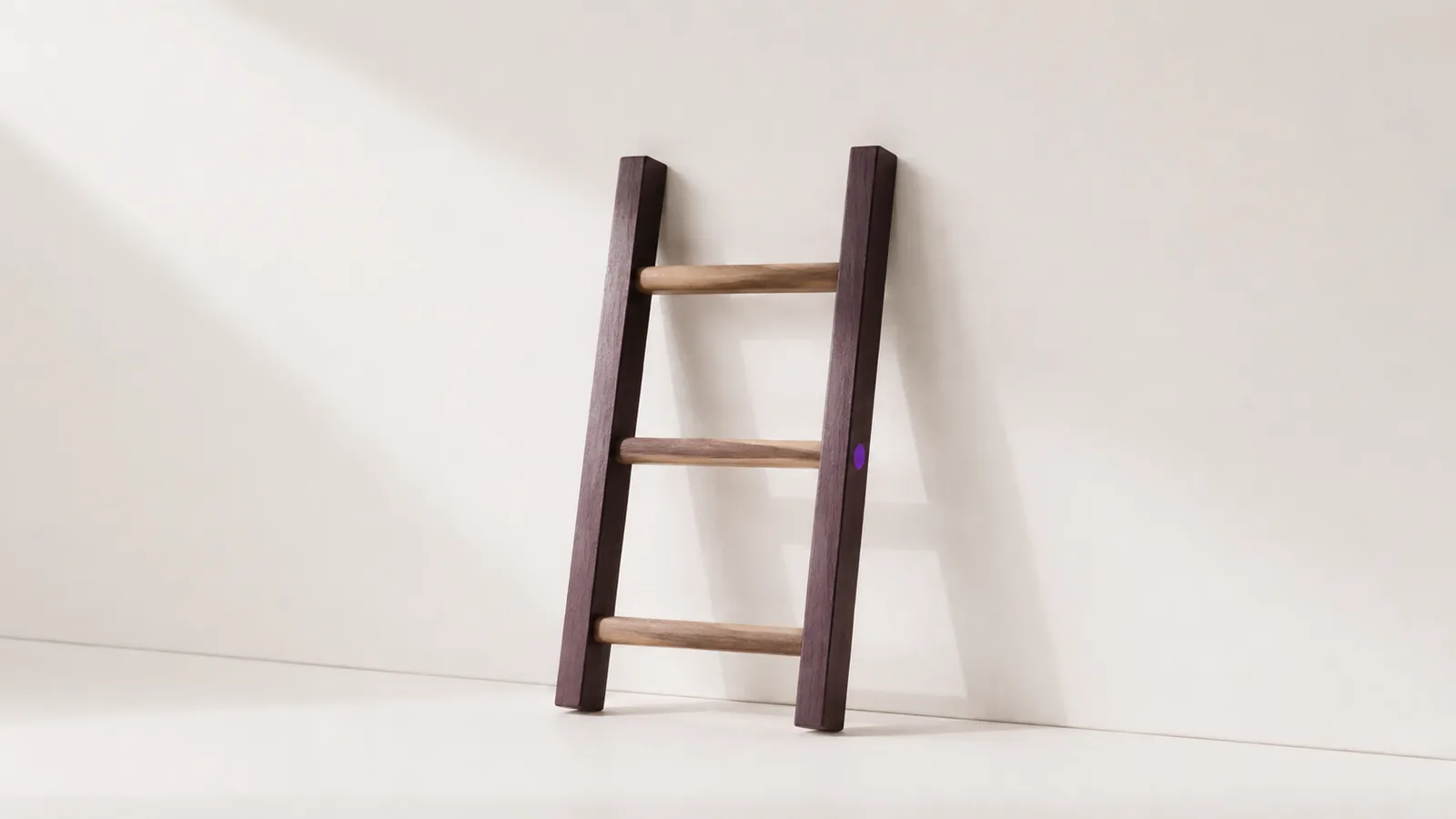 A short ladder with only three rungs standing against a pale wall.