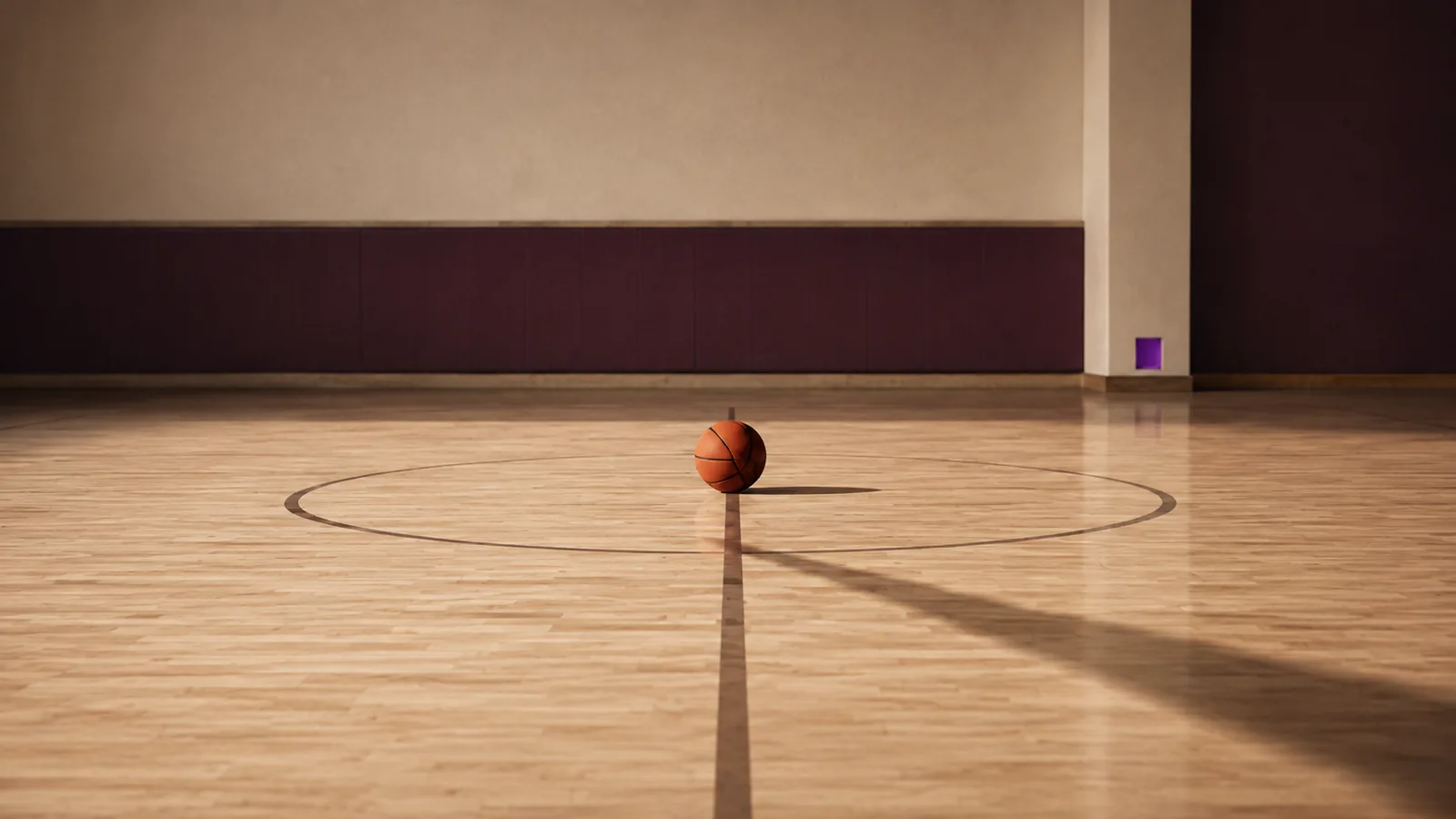 An empty basketball court with a ball at centre and a shadow crossing the floor.