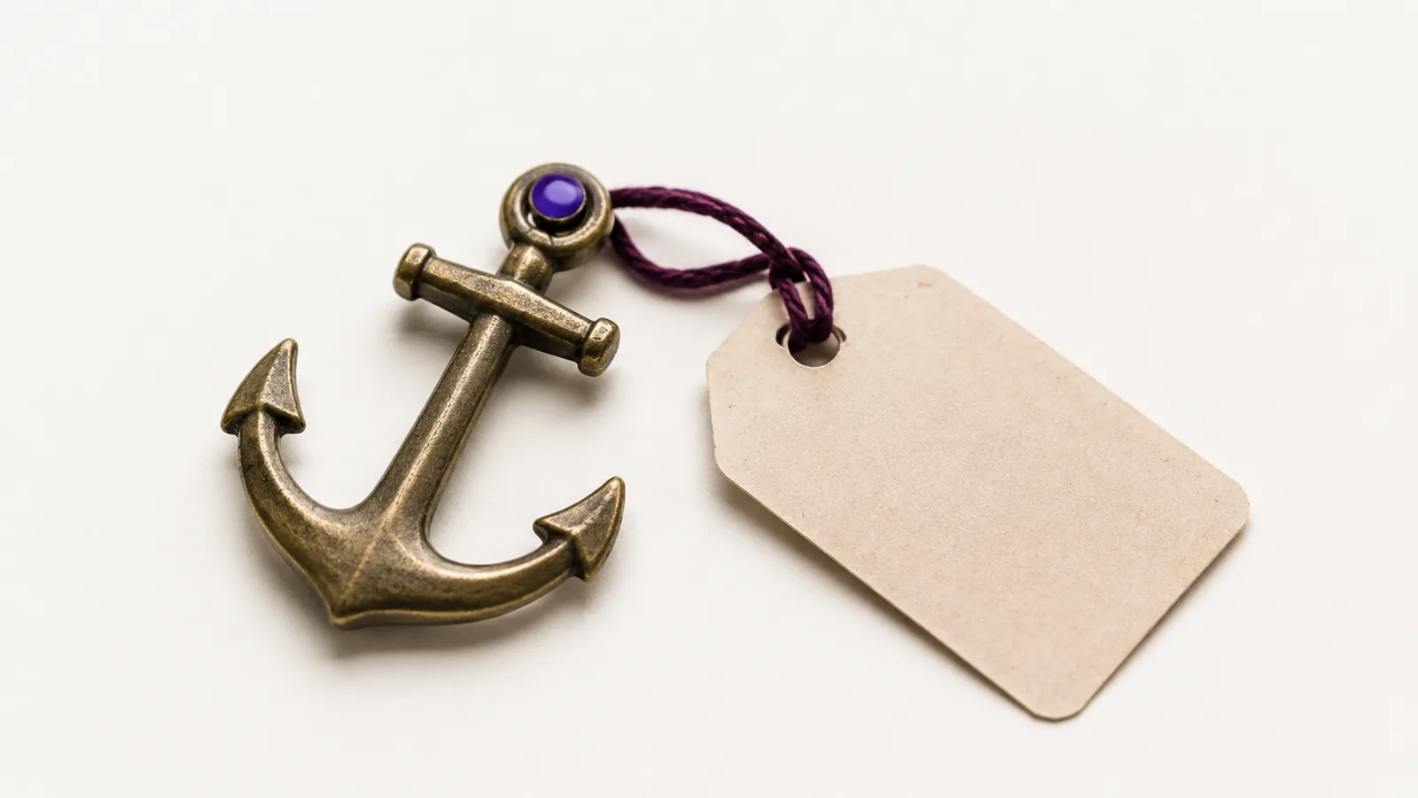 A small brass anchor on a pale surface beside a blank price tag.